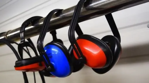 Gehörschutz Kopfhörer in Blau und Rot hängen an einer Metallstange in einer Werkstatt.