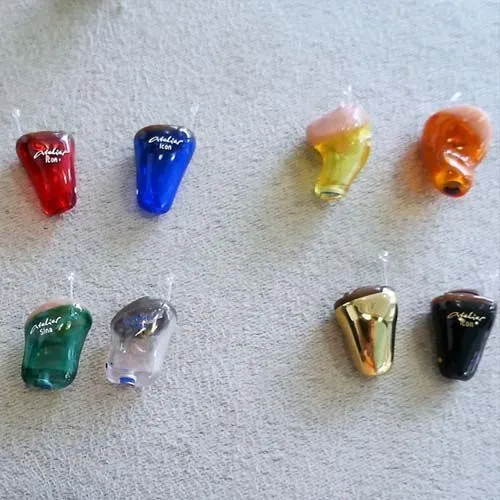 Sechs bunte In-Ear-Monitor-Kopfhörer liegen auf grauem Stoff nebeneinander angeordnet.