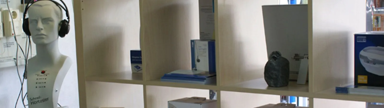 Ein Regal mit Hörtest-Puppe, Kopfhörern und Hörgeräte-Zubehör in einem Akustikerladen.