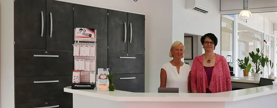 Empfangsbereich einer modernen Arztpraxis mit zwei freundlichen Mitarbeiterinnen am Tresen.